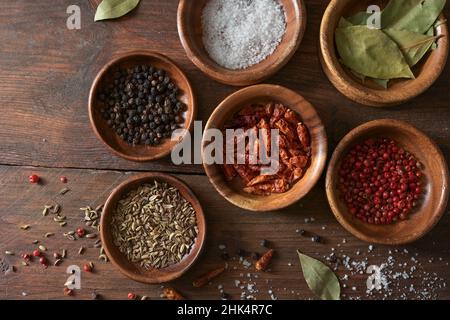 Selezione di spezie secche in piccole ciotole su un rustico tavolo di legno, spazio copia, alto angolo di vista dall'alto Foto Stock