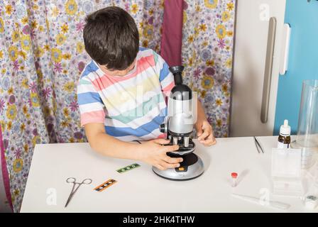 Bambino piccolo ragazzo caucasico guardando attraverso il microscopio a scuola. Foto Stock
