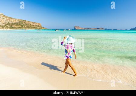 Bella donna con cappello di sole a piedi su idilliaca spiaggia vuota, Creta, Isole Greche, Grecia, Europa Foto Stock