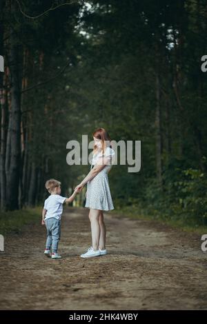 la mamma giovane donna cammina con il bambino piccolo figlio nella mano dei boschi insegna a camminare Foto Stock