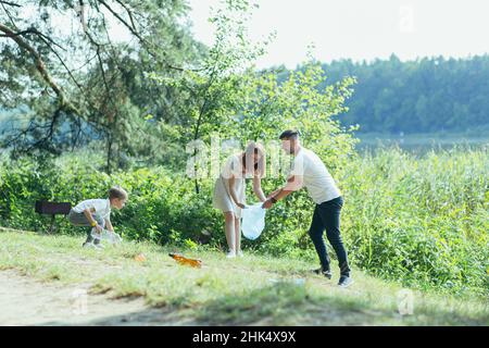 il volontario di famiglia pulisce i rifiuti in natura. Padre e madre, genitori, figli, figli volontari di famiglia in una giornata di sole ripulendo i rifiuti bo Foto Stock