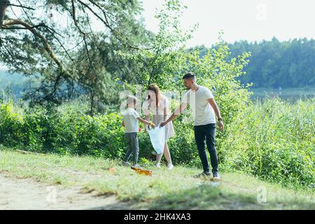 il volontario di famiglia pulisce i rifiuti in natura. Padre e madre, genitori, figli, figli volontari di famiglia in una giornata di sole ripulendo i rifiuti bo Foto Stock