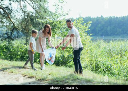 il volontario di famiglia pulisce i rifiuti in natura. Padre e madre, genitori, figli, figli volontari di famiglia in una giornata di sole ripulendo i rifiuti bo Foto Stock