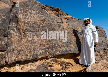 Uomo che punta a sculture di roccia, pietra di Bir Hima Petroglyphs e iscrizioni, patrimonio dell'umanità dell'UNESCO, Najran, Regno dell'Arabia Saudita, Medio Oriente Foto Stock