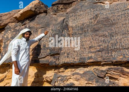 Uomo che punta a sculture di roccia, pietra di Bir Hima Petroglyphs e iscrizioni, patrimonio dell'umanità dell'UNESCO, Najran, Regno dell'Arabia Saudita, Medio Oriente Foto Stock