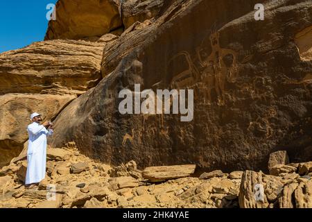 Uomo che punta a sculture di roccia, pietra di Bir Hima Petroglyphs e iscrizioni, patrimonio dell'umanità dell'UNESCO, Najran, Regno dell'Arabia Saudita, Medio Oriente Foto Stock