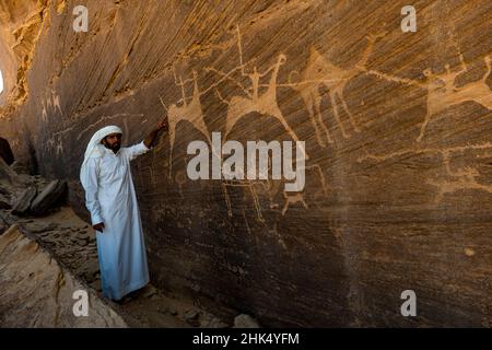 Uomo che punta a sculture di roccia, pietra di Bir Hima Petroglyphs e iscrizioni, patrimonio dell'umanità dell'UNESCO, Najran, Regno dell'Arabia Saudita, Medio Oriente Foto Stock