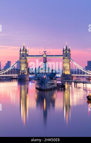 Vista sull'alba di HMS Belfast e Tower Bridge riflessa nel Tamigi, con Canary Wharf sullo sfondo, Londra, Inghilterra, Regno Unito, Europa Foto Stock