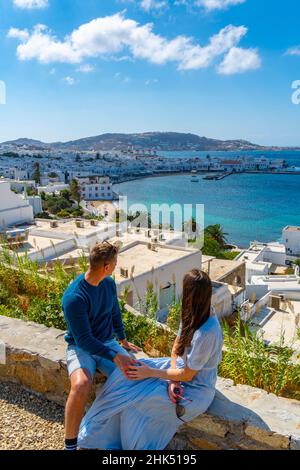 Giovane coppia con vista elevata dei mulini di farina e della città, Mykonos Town, Mykonos, Isole Cicladi, Isole Greche, Mar Egeo, Grecia, Europa Foto Stock