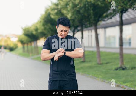 L'atleta asiatico maschile, stanco dopo uno jogging mattutino, corre nel parco vicino allo stadio Foto Stock