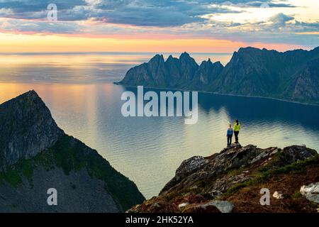 Due giovani donne che osservano il tramonto in piedi sulla cima della montagna, l'isola di Senja, la contea di Troms, la Norvegia, la Scandinavia, Europa Foto Stock