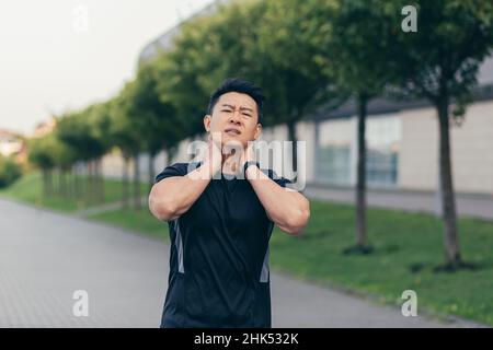 Atleta asiatico maschile, che corre nel parco in uno zaino prima di lavorare, correre nel parco vicino allo stadio ha grave dolore al collo stanco di dolore Foto Stock