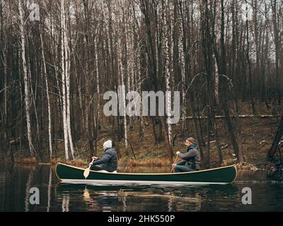 Due uomini che pedalano una canoa verde sul lago della foresta. Stile di vita attivo, bellissimo autunno o primavera foresta scenario Foto Stock