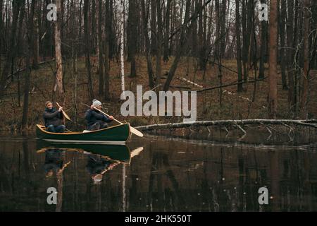 Due uomini che pedalano una canoa verde sul lago della foresta. Stile di vita attivo, bellissimo autunno o primavera foresta scenario Foto Stock