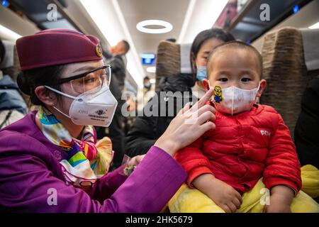 (220202) -- CHONGQING, 2 febbraio 2022 (Xinhua) -- Lin Mengfan mette un adesivo cartoon sulla maschera facciale di un ragazzino a bordo di un treno superveloce Fuxing che viaggia sulla ferrovia di Chendu-Chongqing nella Cina sudoccidentale, 27 gennaio 2022. Nato nel 2000, Lin Mengfan è una nuova superba stazione per un treno superveloce Fuxing sulla ferrovia di Chendu-Chongqing. Nel frattempo, Lin è al servizio della corsa di corsa del festival di primavera per la prima volta nella sua carriera. Nel caso in cui ci sia un passeggero che ha bisogno di aiuto a bordo, Lin ha preparato con lei una custodia versatile per attrezzi. Nella custodia sono presenti adesivi colorati per i passeggeri che segnano il bagaglio Foto Stock