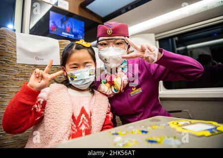 (220202) -- CHONGQING, 2 febbraio 2022 (Xinhua) -- Lin Mengfan si pone per una foto con un piccolo passeggero a bordo di un treno superveloce Fuxing che viaggia sulla ferrovia di Chendu-Chongqing nella Cina sudoccidentale, 27 gennaio 2022. Nato nel 2000, Lin Mengfan è una nuova superba stazione per un treno superveloce Fuxing sulla ferrovia di Chendu-Chongqing. Nel frattempo, Lin è al servizio della corsa di corsa del festival di primavera per la prima volta nella sua carriera. Nel caso in cui ci sia un passeggero che ha bisogno di aiuto a bordo, Lin ha preparato con lei una custodia versatile per attrezzi. Nella custodia sono gli adesivi colorati per i passgenger per marcare i loro bagagli, cartone sti Foto Stock