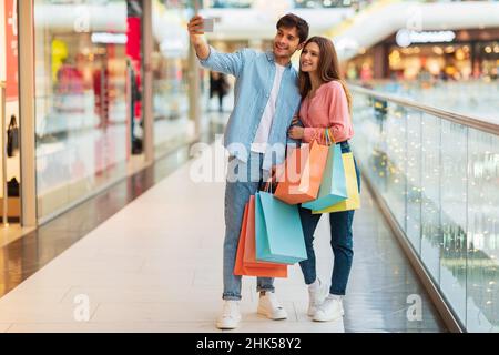 Happy Couple Shopping e fare Selfie al telefono in Mall Foto Stock