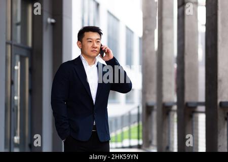 L'uomo d'affari asiatico che parla al telefono serio ha una conversazione arrabbiata Foto Stock