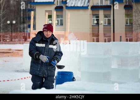 Un lavoratore attira l'acqua da un barile blu con una siviera nel luogo di assemblaggio della città di ghiaccio Foto Stock