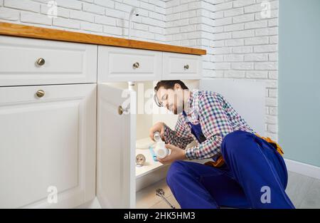 Giovane idraulico professionale serio installa nuovo sifone sotto il lavandino in cucina di appartamento. Foto Stock