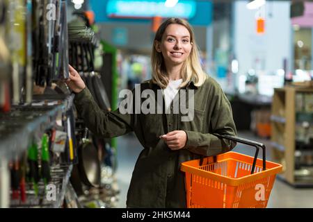 giovane donna caucasica cammina tra file di supermercato con un cestino in mano. Shopping femminile attraverso la sezione merci, navigazione. Grande magazzino con tanto o Foto Stock