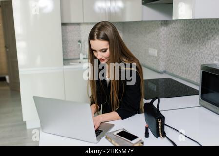 Donna in abito nero sorridente a un computer portatile in cucina Foto Stock