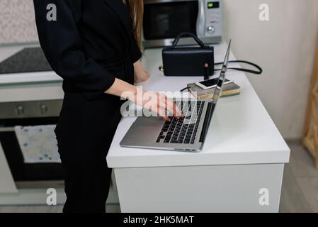 Donna in abito nero sorridente a un computer portatile in cucina Foto Stock