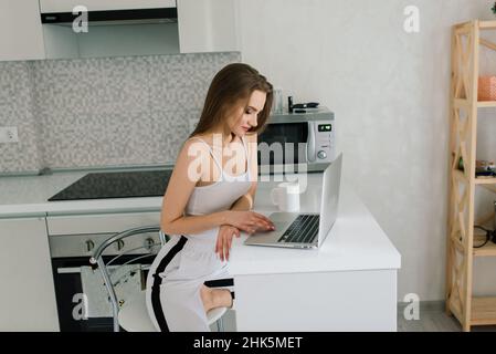 Donna in abito nero sorridente a un computer portatile in cucina Foto Stock