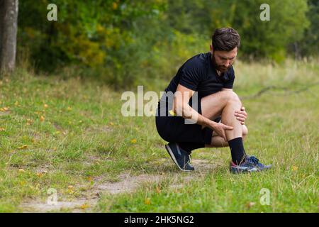 Atleta maschio ferito durante l'allenamento, ha grave dolore alle gambe, dolori muscolari, seduta a terra e urla nel dolore Foto Stock