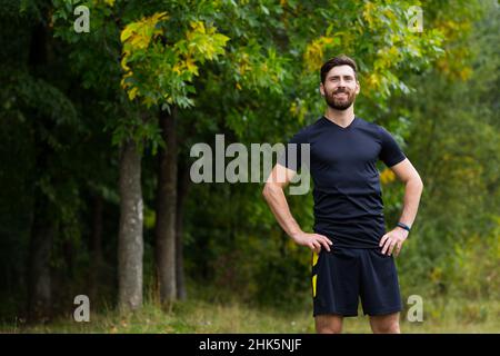 Primo piano ritratto giovane felice uomo bearded in piedi in natura tra alberi di foresta rilassa, respira aria fresca chiudendo gli occhi. Il maschio gode una vita di Foto Stock