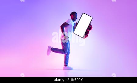 Immagine dello schermo dello smartphone. Positivo giovane uomo nero che corre con cellulare vuoto, consigliando nuova app in neon light Foto Stock