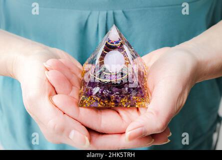 Vista ravvicinata delle mani della donna che tengono e utilizzano Orgonite o Orgone Pyramid a casa durante la meditazione. Convertire energia negativa in energia positiva. Foto Stock