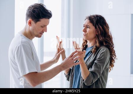 Sposata cricly-capelli donna litigare angrily gesticuling e urlando con marito brunet su problemi di famiglia in piedi in cucina closeup Foto Stock