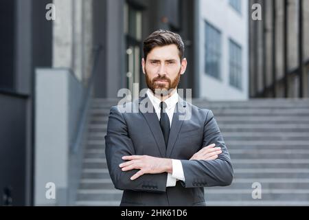 Ritratto giovane fiducioso successo caucasico bearded uomo d'affari guardando fotocamera serio uomo d'affari in piedi su sfondo urbano di ufficio moderno Foto Stock