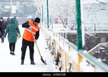 UZHHOROD, UCRAINA - 2 FEBBRAIO 2022 - Un operaio comunale pulisce un ponte pedonale attraverso il fiume Uzh dalla neve con una pala in inverno, Uzhho Foto Stock