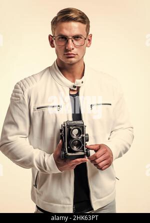 Il desiderio incontra un nuovo hobby. Bel ragazzo tenere retro fotocamera isolato su bianco. I giovani fotografi indossano occhiali in stile casual. Attrezzatura fotografica Foto Stock