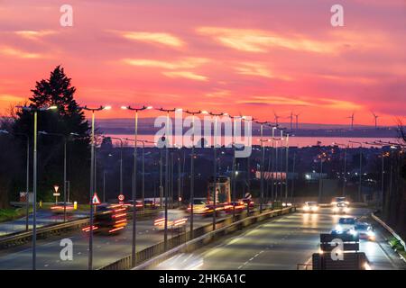 Spettacolare cielo rosso serale dopo il tramonto sulla Thanet Way, A299, una strada a due corsie che collega il Nord Est del Kent con il M2 e Londra. Sullo sfondo c'è l'isola di Sheppey e alcune turbine eoliche. Ora di punta con traffico sulla strada. Foto Stock