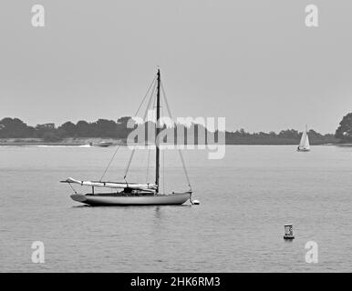 Una sola barca con una vela a Lewis Bay a Cape Cod, Massachusetts.USA, in una giornata grigia. Vicino al porto di Hyannis. In bianco e nero. Foto Stock
