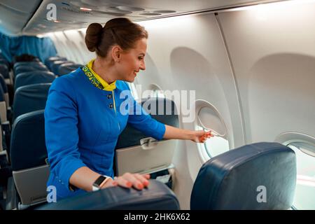 Donna sorridente stewardess chiusura finestra in aereo Foto Stock