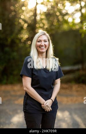 Un professionista medico con scrubbst nero con capelli biondi lunghi all'esterno in uno sfondo naturale con spazio copia Foto Stock