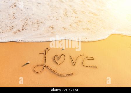 Parola 'Amore' scritta sulla sabbia della spiaggia. Messaggio romantico scritto sulla riva al tramonto Foto Stock