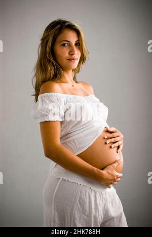 Ritratto di giovane donna ispanica incinta, in piedi lateralmente, tenendo la pancia Foto Stock