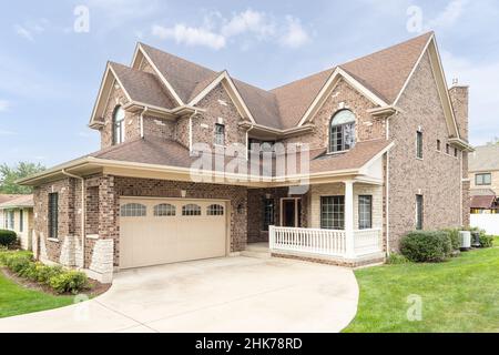 Una casa a due piani in mattoni e pietra con veranda anteriore coperta e garage a due porte. Foto Stock