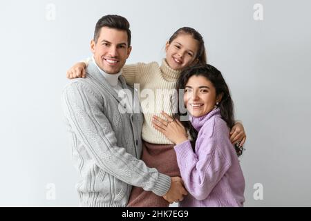 Ragazza piccola felice e i suoi genitori in maglioni caldi su sfondo chiaro Foto Stock