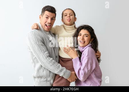 Bambina e i suoi genitori in maglioni caldi che mostrano lingue su sfondo chiaro Foto Stock