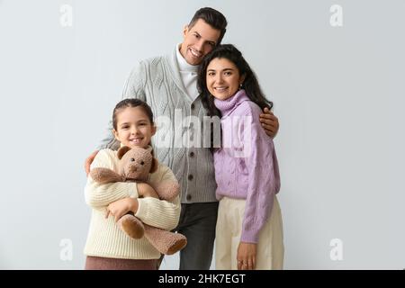 Bambina con giocattolo e i suoi genitori in maglioni caldi su sfondo chiaro Foto Stock