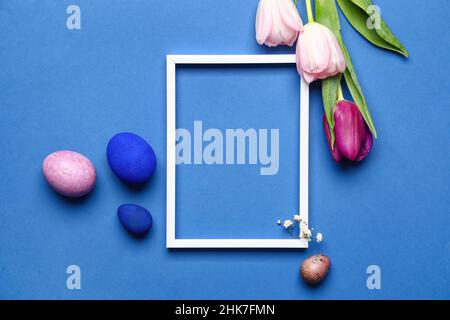 Composizione pasquale con cornice bianca, uova e fiori su sfondo blu Foto Stock