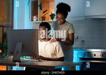 Amorevole moglie sostegno freelance web designer marito che lavora su un progetto di piccola impresa da casa tardi Foto Stock