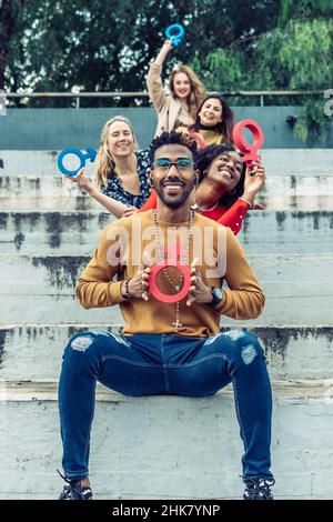 un uomo nero sorridente mostra alla telecamera un simbolo femminista capovolto come se fosse una croce cattolica Foto Stock