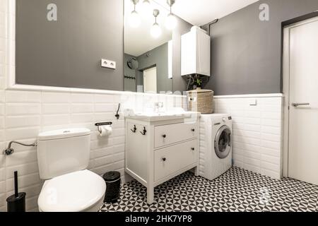 Servizi igienici decorati in stile contemporaneo con pavimenti idraulici, lavabo bianco, lavatrice e riscaldatore sulla parte superiore Foto Stock